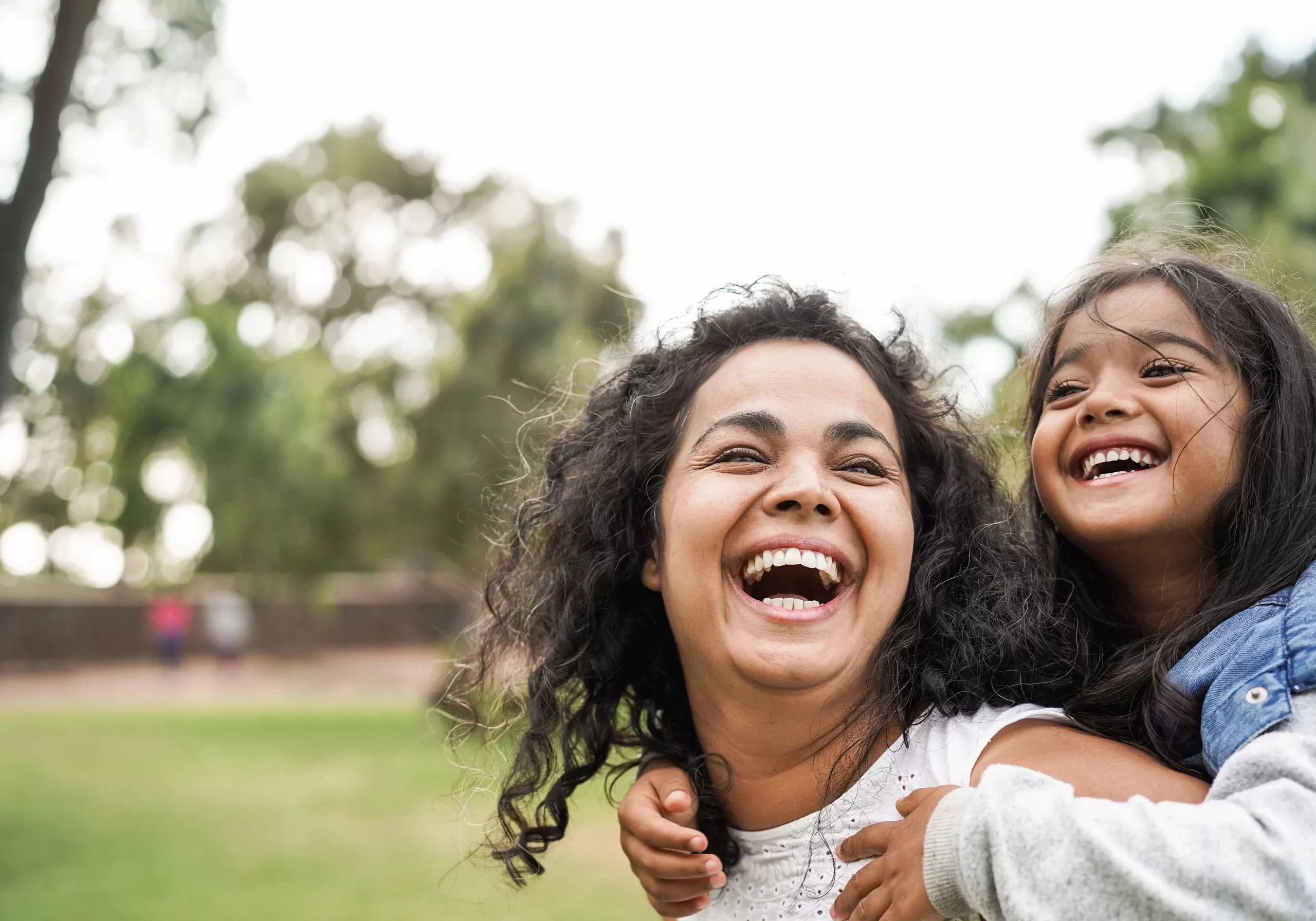 Mother piggy backing daughter, both laughing and smiling.