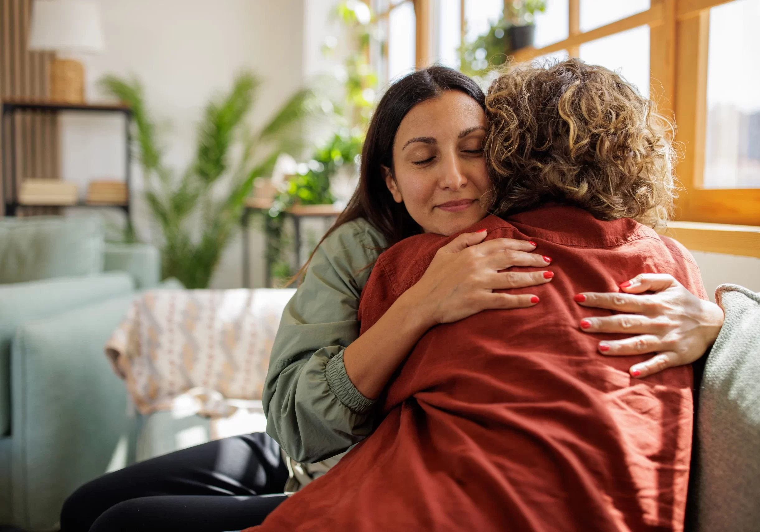 Two women sitting on lounge embracing eachother.