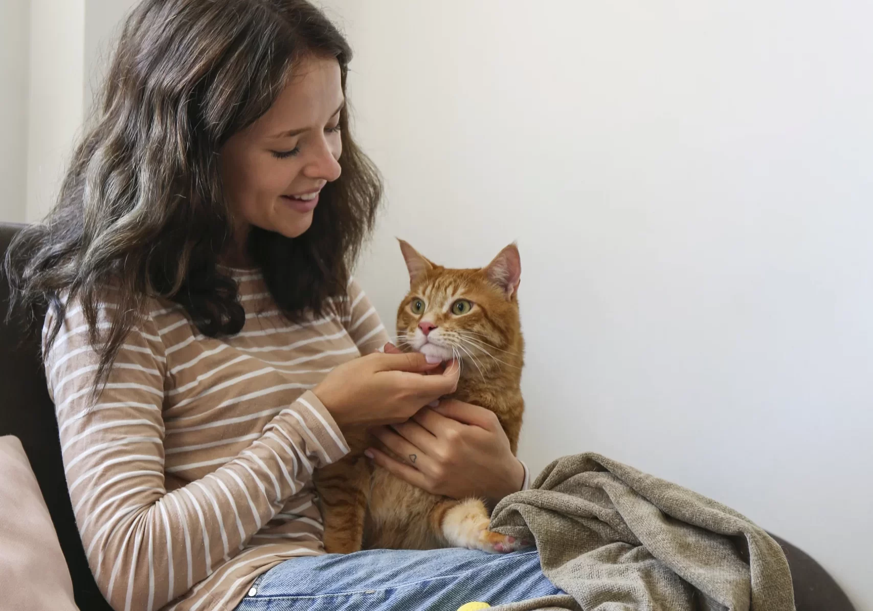 Young girl smiling, looking down at a ginger cat sitting on her lap.
